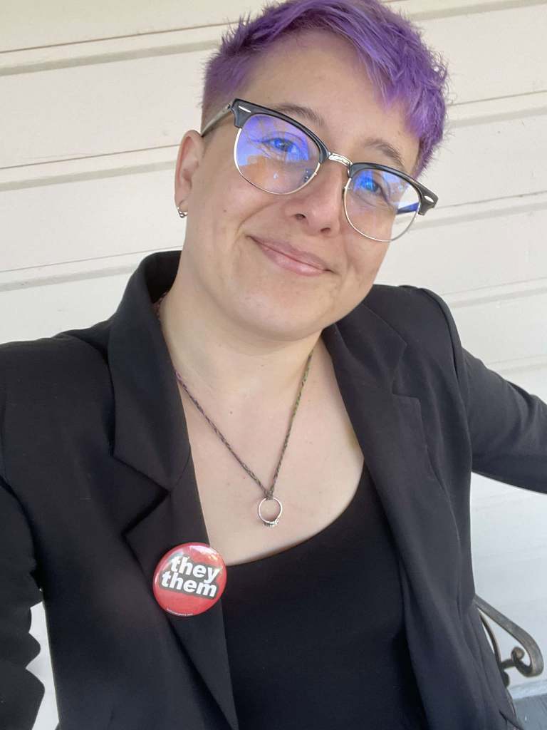 Picture of Daisy Ahlstone with purple hair, glasses, and wearing a suit jacket smiling.